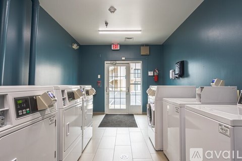 A row of washing machines in a laundromat with an exit sign above the door.
