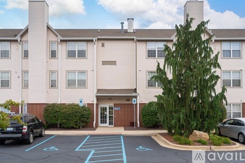 A parking lot in front of a building with a tree and a car parked.