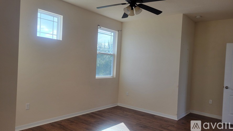 A room with a ceiling fan and two windows.