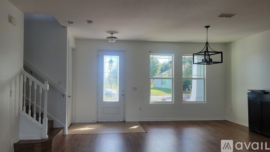 A room with a staircase on the left and a chandelier hanging from the ceiling.