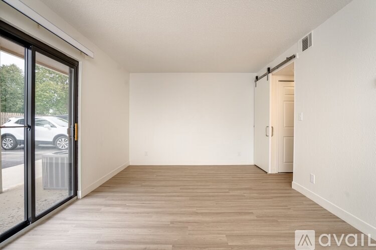 A room with wooden flooring and white walls, with a door on the right and a sliding glass door on the left.