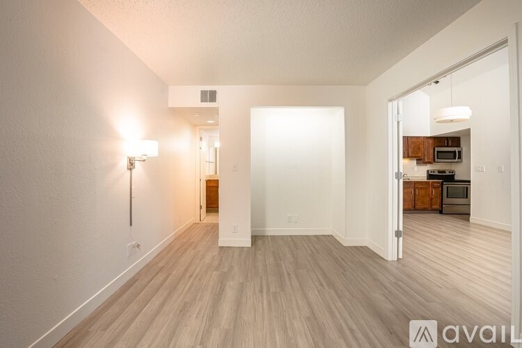 A room with wooden flooring and a white door leading to a kitchen.