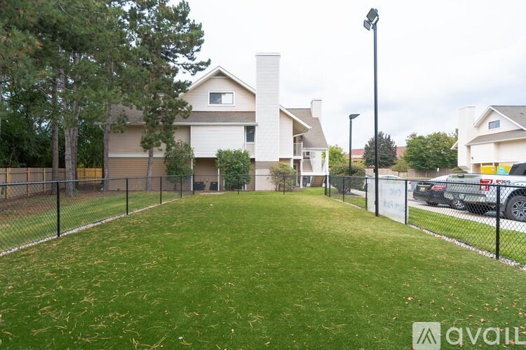 A grassy area in front of a house with a fence and a car parked in the driveway.