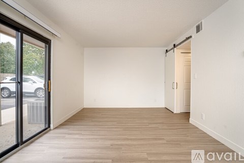 A room with wooden flooring and white walls, with a door on the right and a sliding glass door on the left.