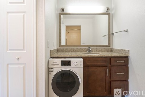 A washing machine is sitting in a laundry room next to a mirror.