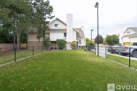 A grassy area in front of a house with a fence and a car parked in the driveway.