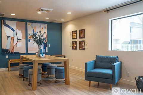 A blue chair sits in a room with a wooden table and a vase of flowers on it.