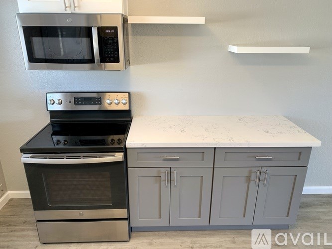 A kitchen with a black oven and microwave above a counter with a white marble top and grey cabinets.