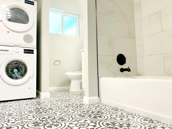 A bathroom with a white tub, toilet, and washing machine.