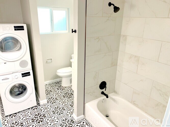 A white washing machine sits next to a white toilet in a bathroom.