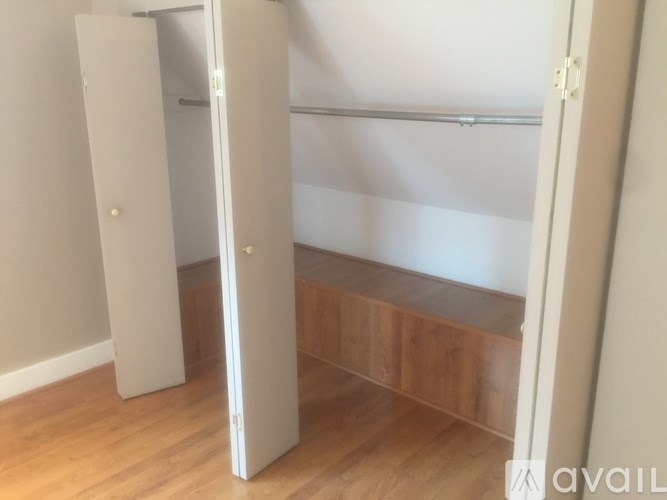 A white closet with a wooden shelf and a white door.