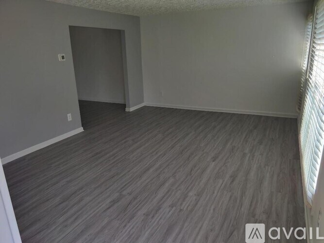 A room with grey flooring and a window with blinds.