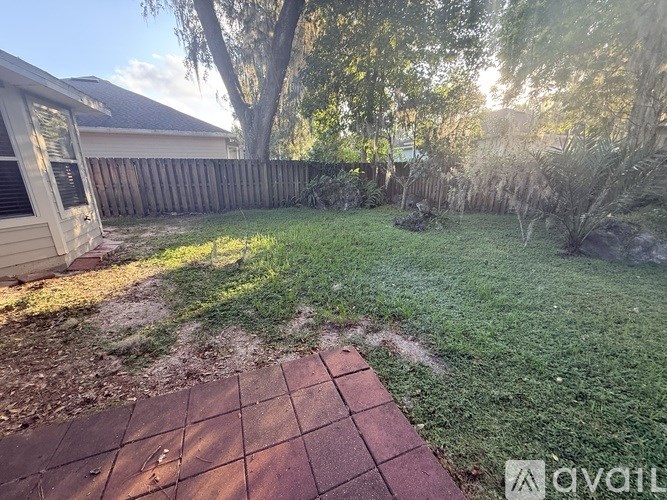 A backyard with a brick patio and a wooden fence.