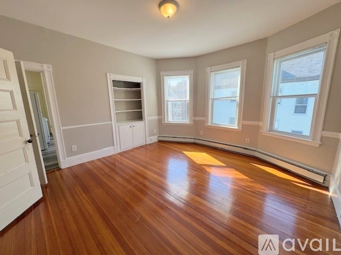 A room with wooden floors and white walls, with a window on the right side.
