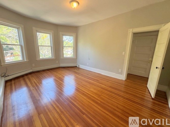 A room with wooden flooring and three windows.