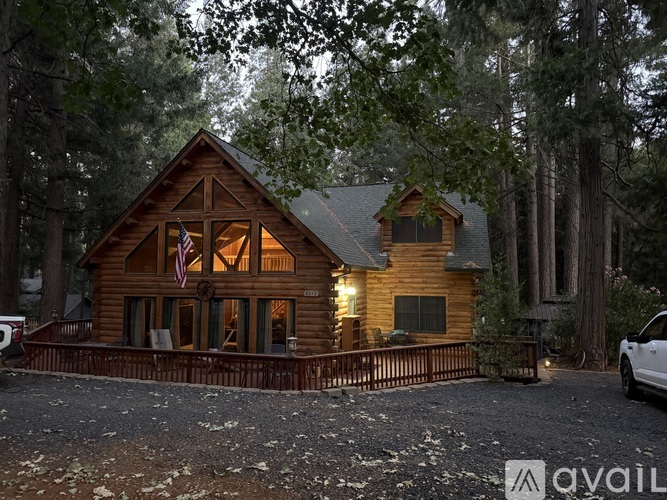 A wooden cabin with a flag on the front porch is surrounded by trees.