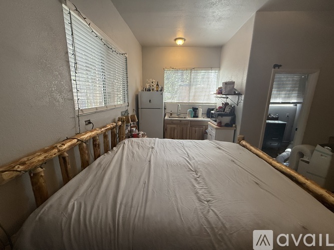 A bedroom with a large bed in the center and a kitchen area in the background.