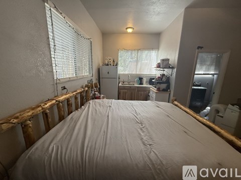 A bedroom with a large bed in the center and a kitchen area in the background.