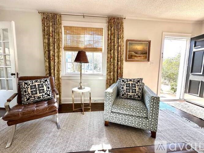 A living room with a brown leather sofa, a grey floral armchair, and a small table with a lamp.