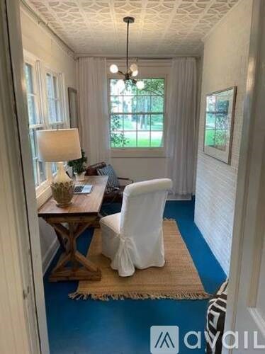 A room with a white chair and a wooden table with a lamp on it.