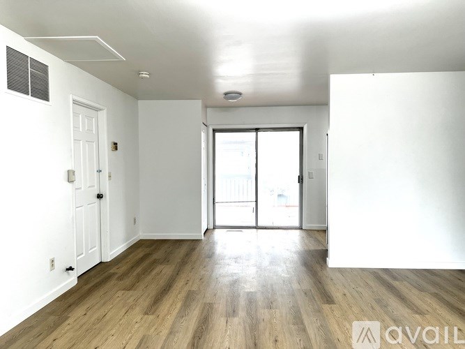 A spacious room with wooden flooring and white walls.