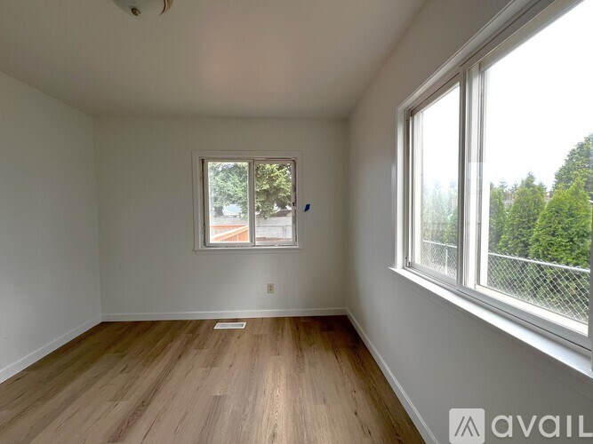 A room with wooden flooring and two windows.