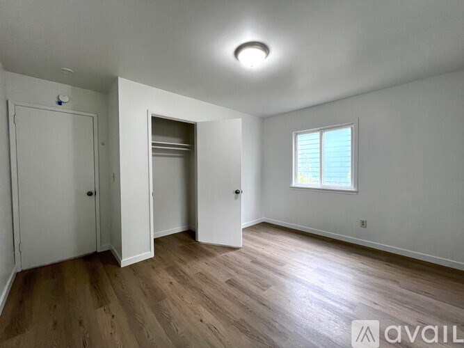 A room with a white door, a window with blinds, and a wooden floor.