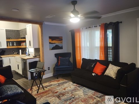 A living room with a black couch and orange curtains.