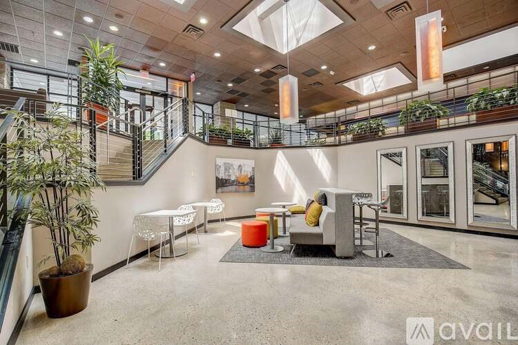 A spacious atrium with a staircase, seating area, and hanging plants.