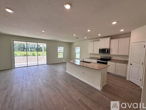 A spacious kitchen and living room with wood flooring and white cabinetry.