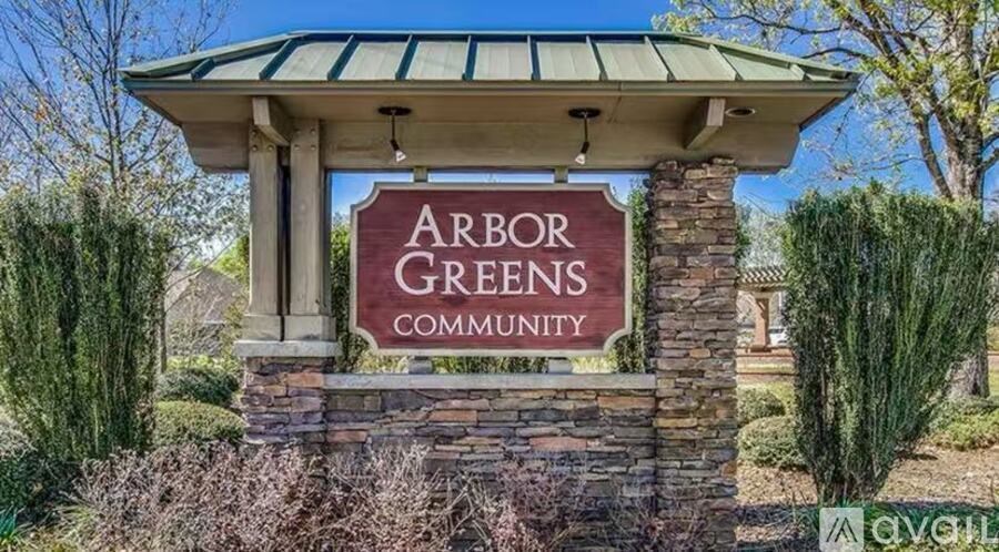 A sign for Arbor Greens Community stands in front of a hedge.