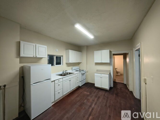 A kitchen with white appliances and cabinets, a sink, and a wooden floor.