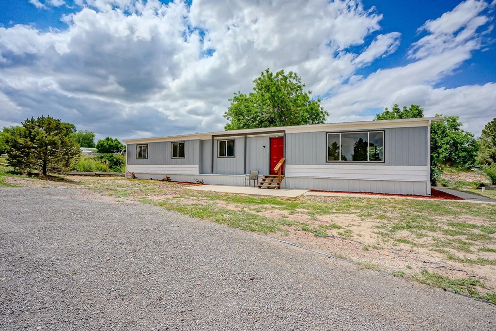 A grey house with a red door stands in a grassy area.