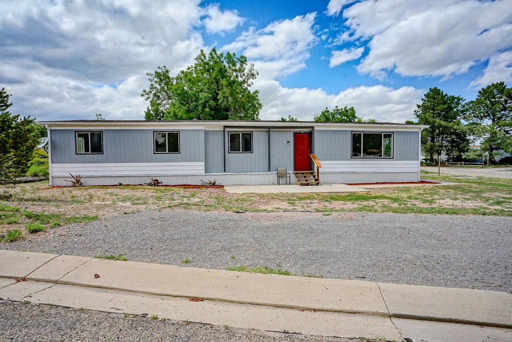 A small house with a red door is surrounded by a gravel driveway.