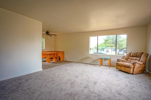 A living room with a carpeted floor and a ceiling fan.