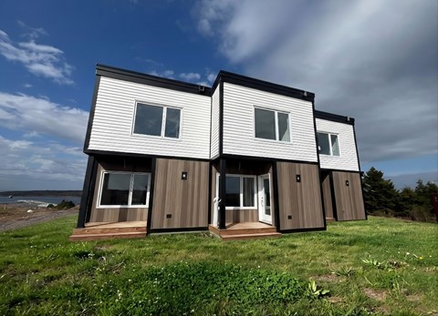 Two houses with white and brown siding are situated on a grassy area.