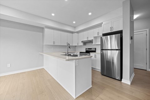 A modern kitchen with a stainless steel refrigerator and wooden flooring.
