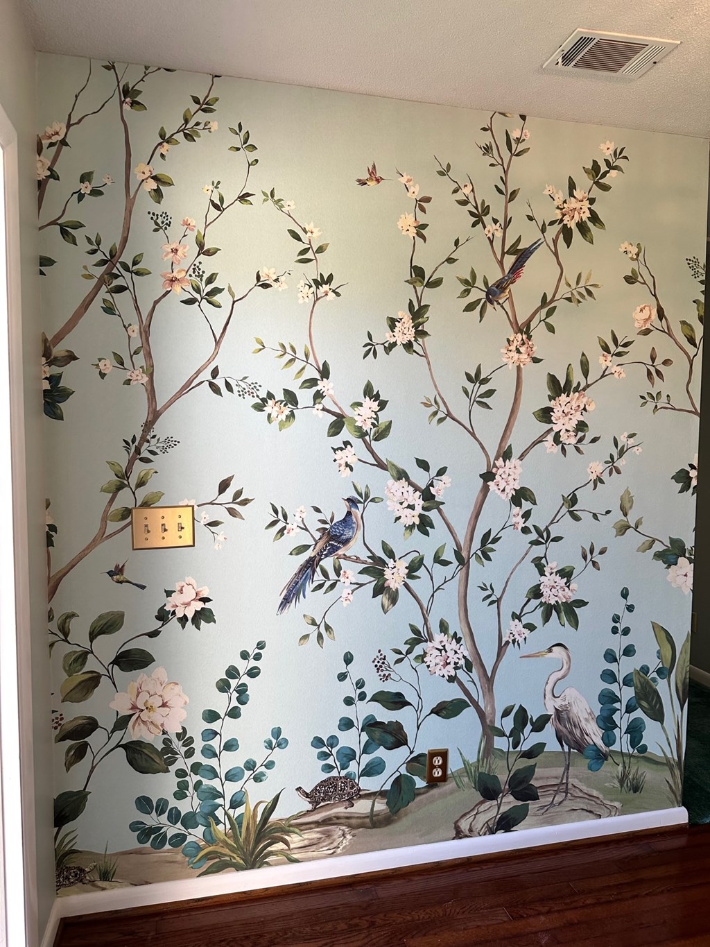 A wall mural of a tree with birds and flowers.