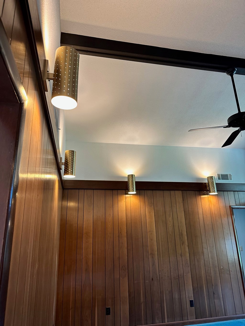 A ceiling fan hangs over a wooden wall.