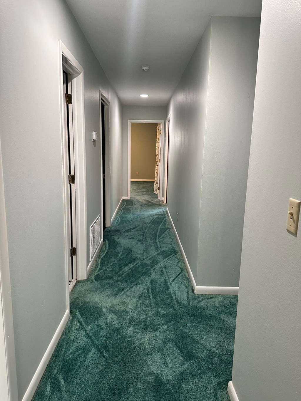 A long hallway with a green carpet and white walls.