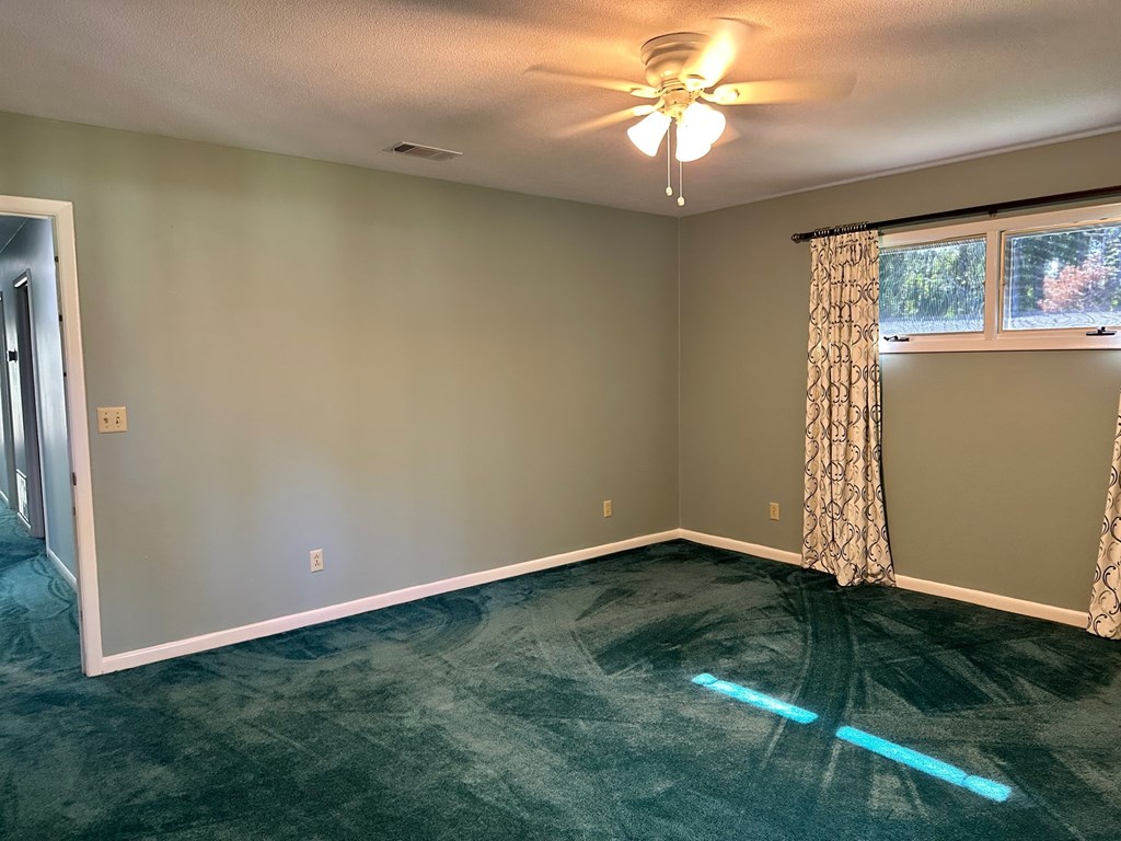 A room with a ceiling fan and a window with curtains.