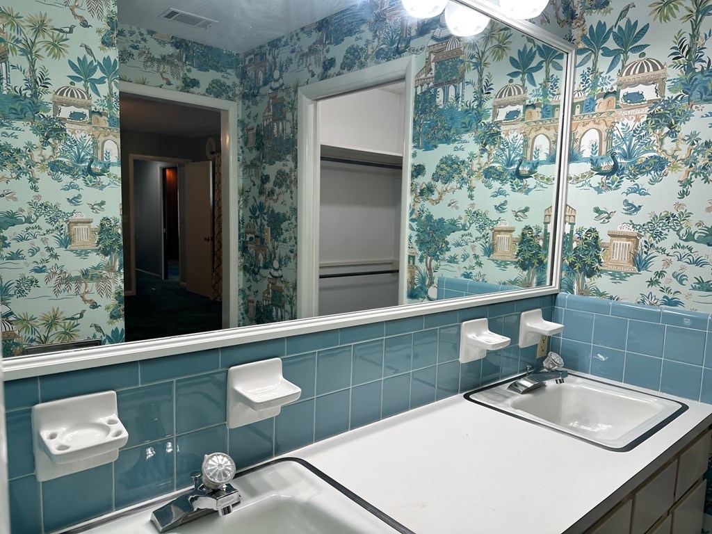A bathroom with a sink, mirror, and wallpaper.