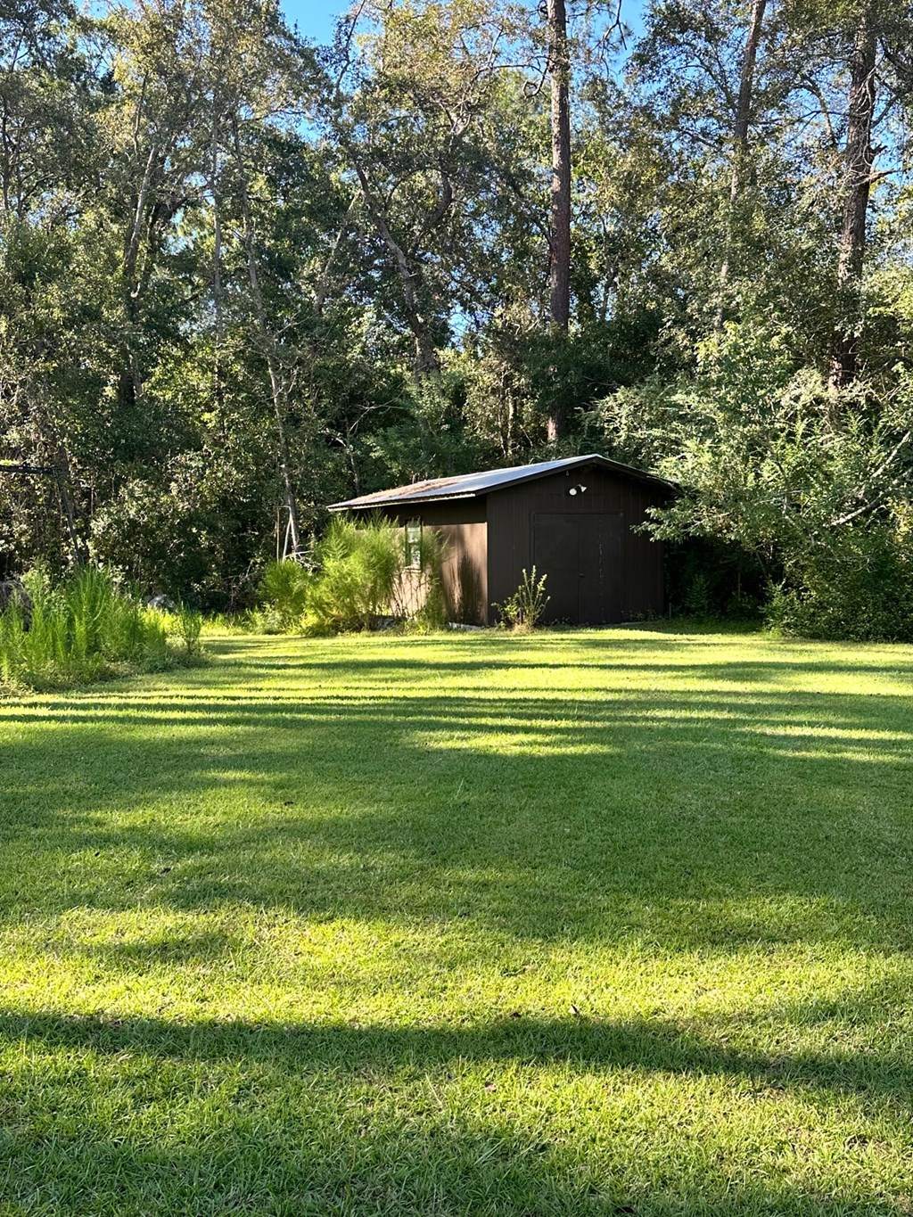 A small building sits in a grassy field with trees in the background.