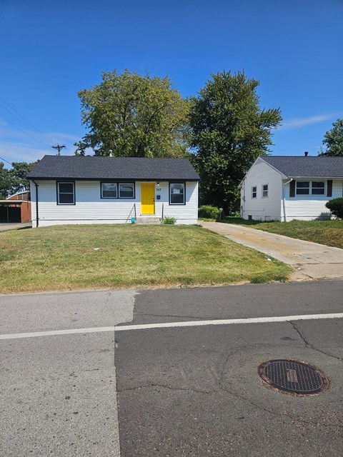 A small white house with a yellow door is situated on a street.