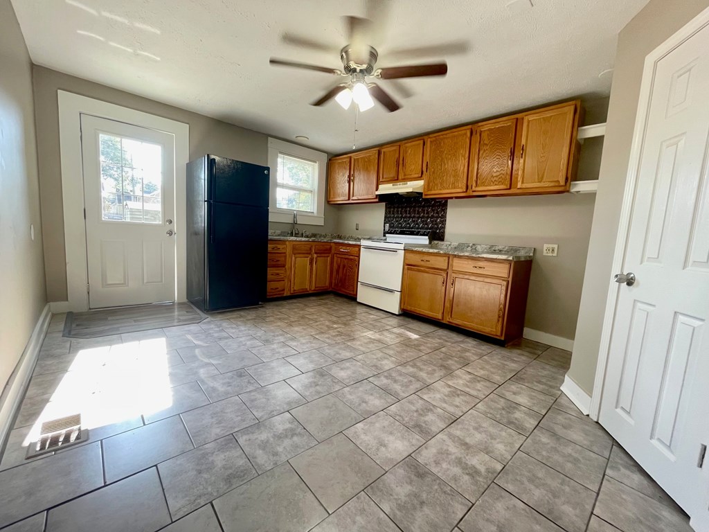 A kitchen with a black fridge, wooden cabinets, and a ceiling fan.