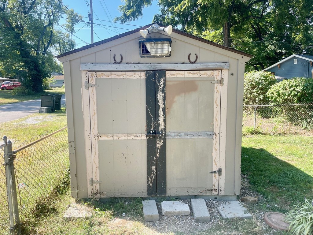 A small, old shed with a black door and a white door is surrounded by a fence.