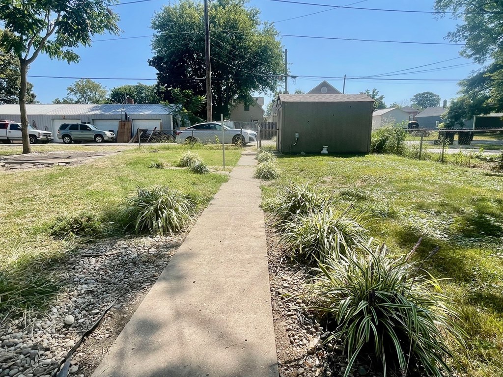 A concrete pathway leads through a grassy area with a utility box on the right.