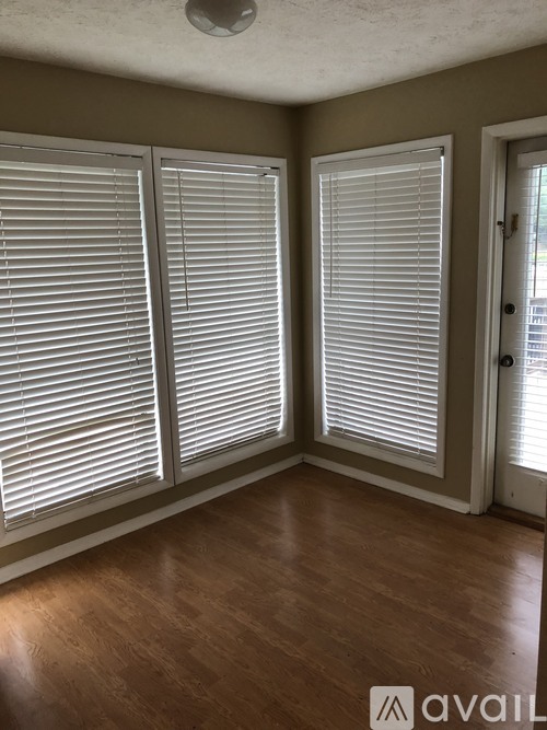 A room with wooden floors and white blinds on the windows.