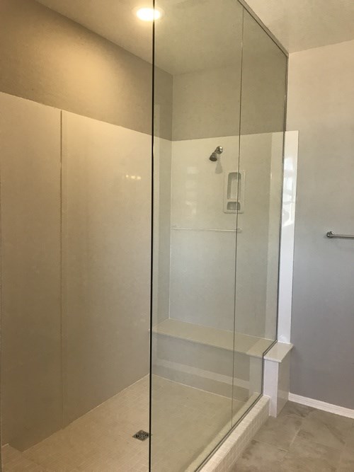 A glass shower stall with a white bench seat.