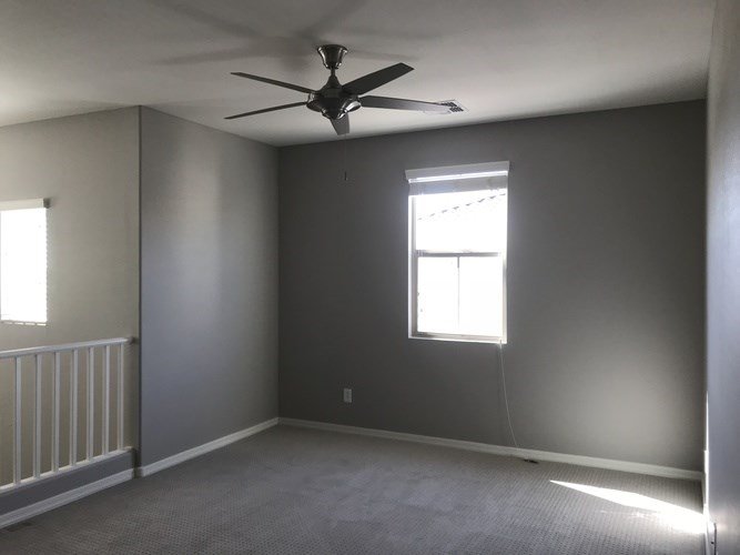 A room with a ceiling fan and a window letting in sunlight.